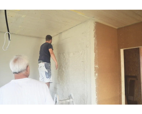 Zwei Handwerker verputzen eine Wand im Innenbereich.