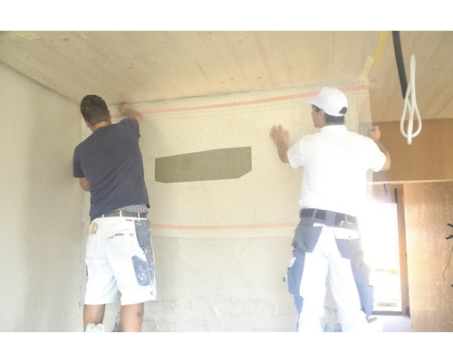 Zwei Handwerker befestigen Armierungsgewebe an einer Wand, die mit einer Schutzfolie versehen ist.