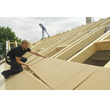 Handwerker verlegt Holzfaserplatten auf einem Dachstuhl.