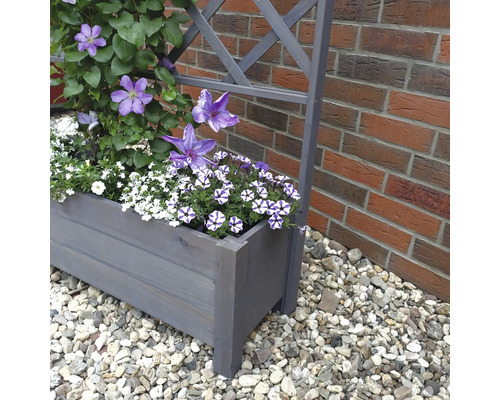 Holzpflanzkasten mit Rankhilfe und blühenden Pflanzen vor einer Backsteinmauer