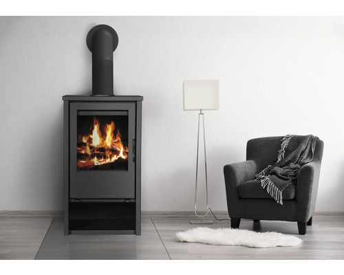 Kaminofen mit brennendem Holz neben Sessel und Stehlampe