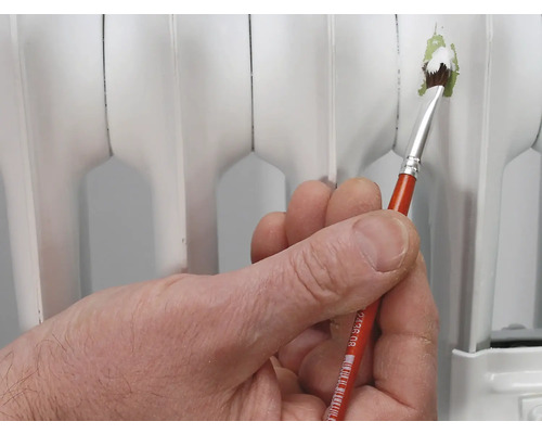 Eine Hand hält einen Pinsel, um einen Heizkörper zu lackieren.