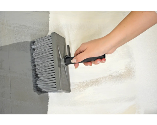 Eine Person streicht eine Wand mit einer Flächenbürste.