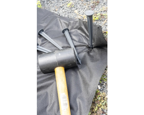 Gartenvlies wird mit einem Gummihammer und Erdankern befestigt.