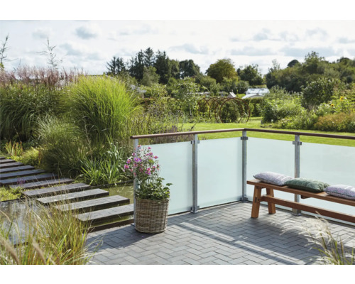 Terrasse mit Sichtschutzwand aus Glas, Bank und Bepflanzung in einem Garten.
