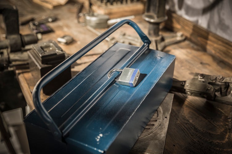 Blaue Werkzeugkiste aus Metall mit einem ABUS Vorhängeschloss auf einer hölzernen Werkbank in einer Werkstatt.