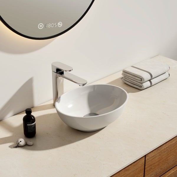 Modernes Badezimmer mit weißem ovalem Aufsatzwaschbecken, verchromter Armatur und hinterleuchtetem Rundspiegel auf heller Arbeitsplatte.