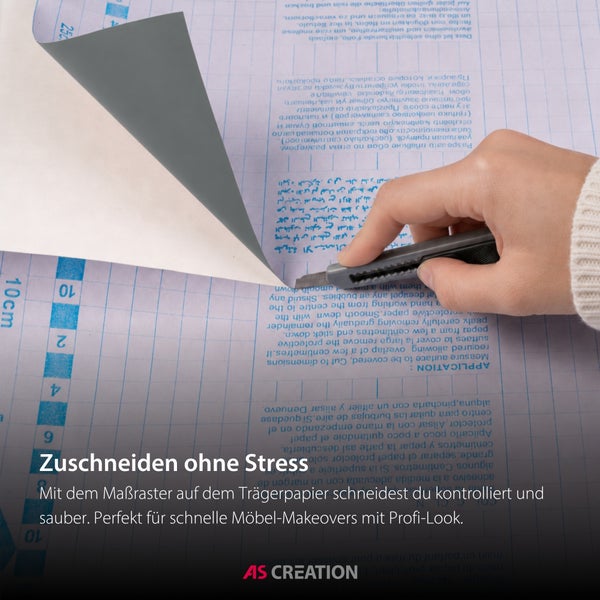Hand schneidet Klebefolie mit einem Cuttermesser auf dem Zentimeterraster des Trägerpapiers zu. AS Creation Logo.