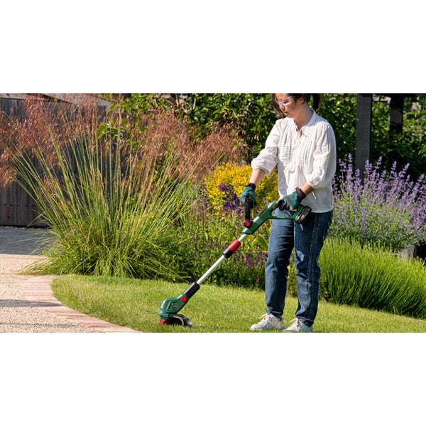 Eine Person benutzt einen Bosch Akku Rasentrimmer zur Rasenkantenpflege in einem Garten.
