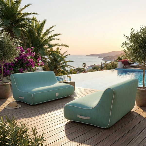 Zwei moderne Outdoor-Loungesessel auf einer Holzterrasse am Infinity-Pool mit Meerblick, umgeben von Palmen und Pflanzen.