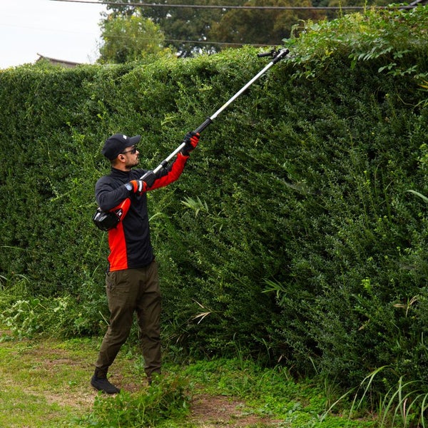 Mann schneidet eine Hecke mit einer Akku-Teleskop-Heckenschere