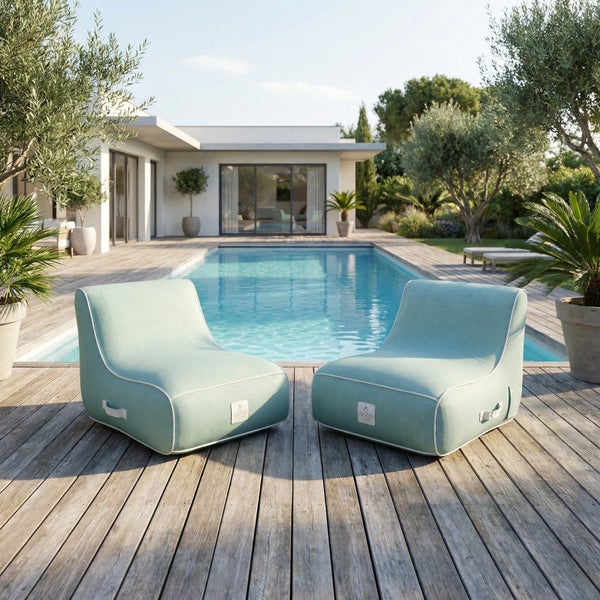 Zwei Outdoor-Lounge-Sessel auf einem Holzdeck neben einem Pool. Helle und geräumige Szene mit moderner Villa und Pflanzen.