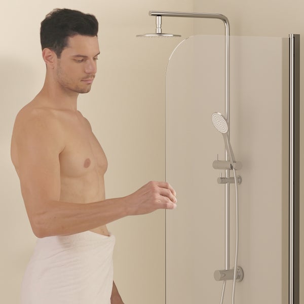Mann mit Handtuch vor Duschwand mit Kopfbrause und Handbrause.