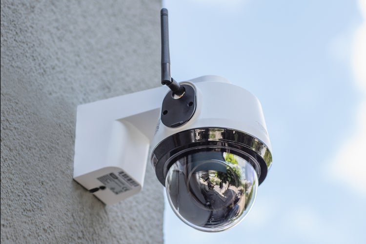Weiße drahtlose Überwachungskamera in Dome-Bauform für den Außenbereich mit Antenne, an einer Wand montiert.