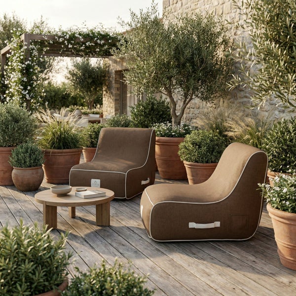 Zwei braune Outdoor-Loungesessel mit weißer Paspelierung auf einer Holzterrasse mit Pflanzen in Terrakottatöpfen und einem niedrigen Holztisch.