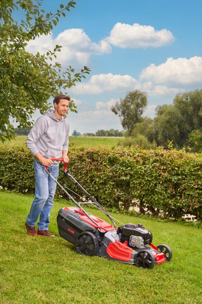 Ein Mann mäht mit einem AL-KO Benzinrasenmäher eine Rasenfläche in einem Garten an einem sonnigen Tag.