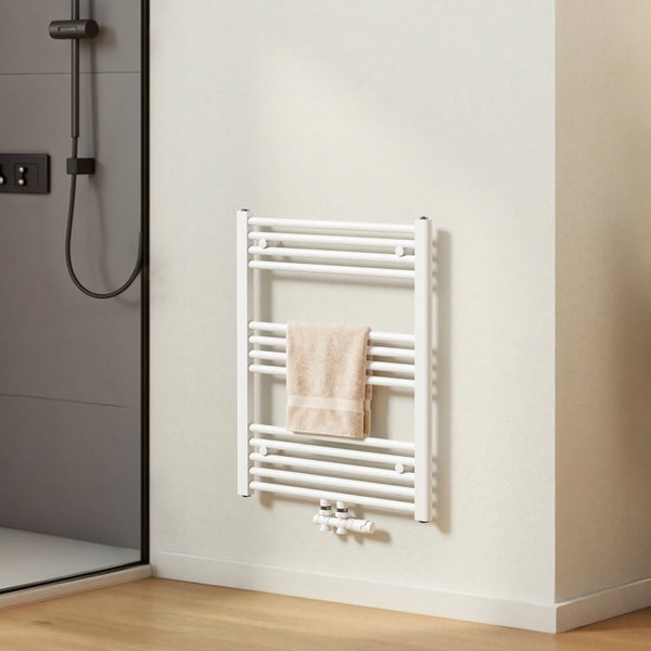 Weißer Handtuchheizkörper an einer Wand im Badezimmer mit einem beigen Handtuch.