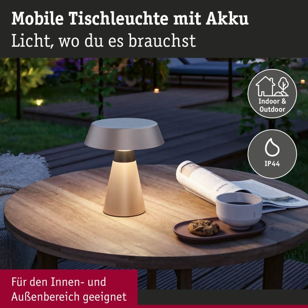 Akkubetriebene Tischleuchte auf einem Tisch im Außenbereich mit Tasse, Gebäck und Zeitung