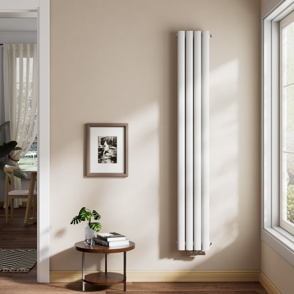 Moderner vertikaler Heizkörper mit vier weißen Rundrohren in einem hellen Wohnzimmer neben einem runden Beistelltisch und einem Fenster.