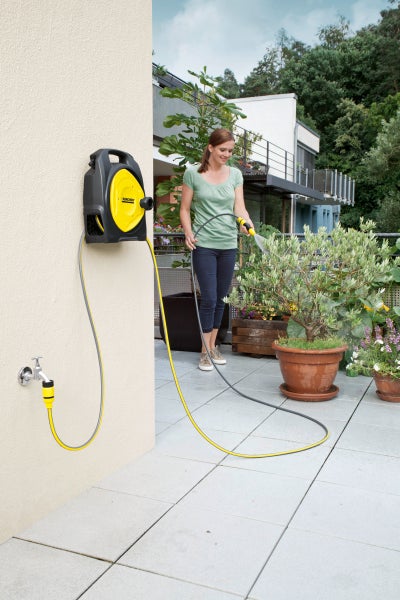 Frau bewässert Pflanzen mit einer Kärcher Schlauchbox auf einer Terrasse.