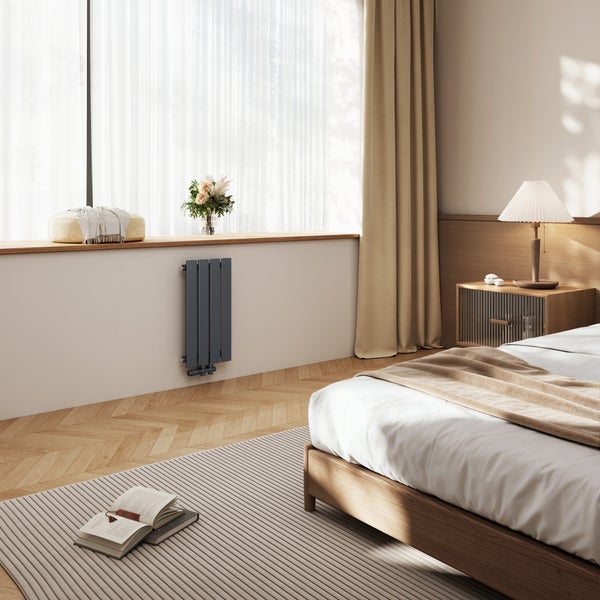 Ein moderner vertikaler Designheizkörper im Schlafzimmer neben einem Fenster mit Holzbank und beige Einrichtung.
