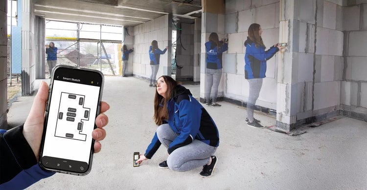 Frau vermisst Raummaße mit einem Laserentfernungsmesser und einem Smartphone in einem Rohbau