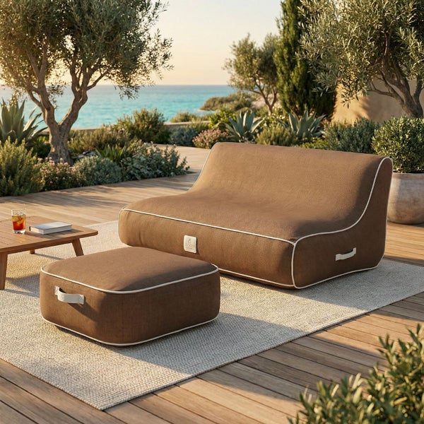 Braunes Outdoor-Lounge-Sofa und Hocker aus Stoff auf einer hellen Holzterrasse mit Pflanzen und Meerblick.