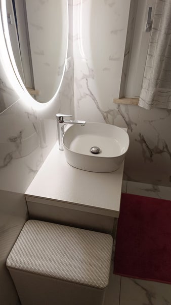 Modernes Badezimmer mit Waschtisch, Aufsatzwaschbecken, Wasserhahn und rundem beleuchtetem Spiegel vor gefliesten Marmorwänden.