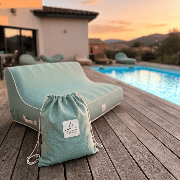 Moderner türkisfarbener Outdoor-Sitzsack mit Tragebeutel auf einer Holzterrasse am Pool. Coco Lounge Logo.