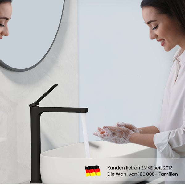 Modernes Badezimmer mit schwarzer Waschtischarmatur, rundem Spiegel und Frau beim Händewaschen