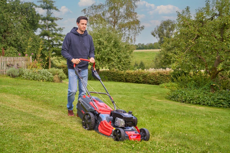 Ein Mann mäht mit einem AL-KO Benzin Rasenmäher einen Rasen in einem Garten.