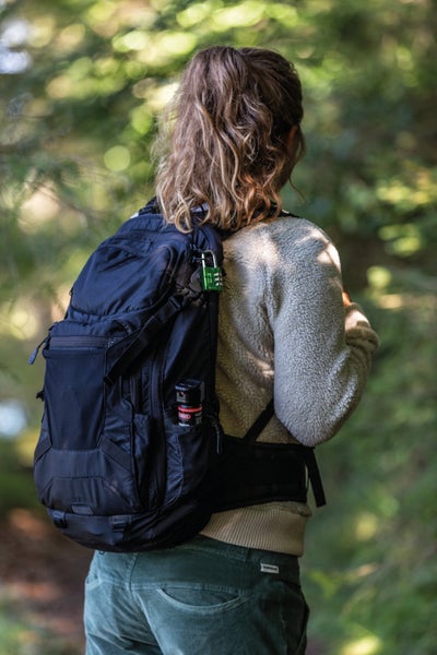 ABUS Pfefferspray in der Seitentasche eines Rucksacks und ABUS Zahlenschloss am Reißverschluss während einer Wanderung.