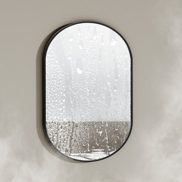 Ovaler Badezimmerspiegel mit schwarzem Rahmen und beschlagener Glasoberfläche an einer Wand.