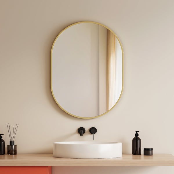 Ovaler Wandspiegel mit goldfarbenem Rahmen über einem weißen Aufsatzwaschbecken und einer schwarzen Wandarmatur in einem modernen Badezimmer.