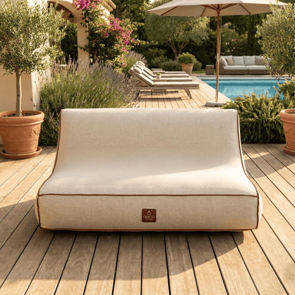 Outdoor-Lounge-Sofa mit Textilbezug und Paspelierung auf einer Holzterrasse neben einem Pool und Gartenpflanzen.