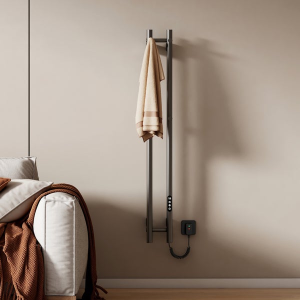 Anthrazitfarbener vertikaler elektrischer Handtuchheizkörper mit digitaler Anzeige, montiert an einer Wand neben einem Sofa mit Kissen und Decke.