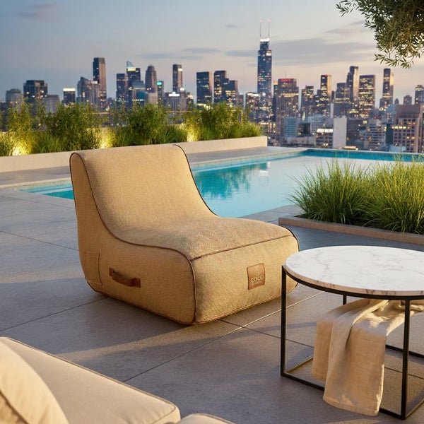 Moderner Outdoor-Loungesessel aus beigem Textil auf einer Dachterrasse mit Pool, Beistelltisch und Skyline.