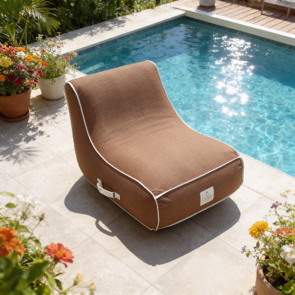 Brauner Outdoor-Sitzsack mit weißer Paspelierung auf einer hellen Steinterrasse neben einem Swimmingpool.
