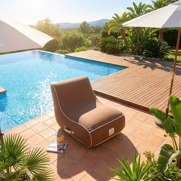 Brauner Outdoor-Sitzsack auf einer Fliesenterrasse an einem Swimmingpool mit Holzdeck und Sonnenschirmen.