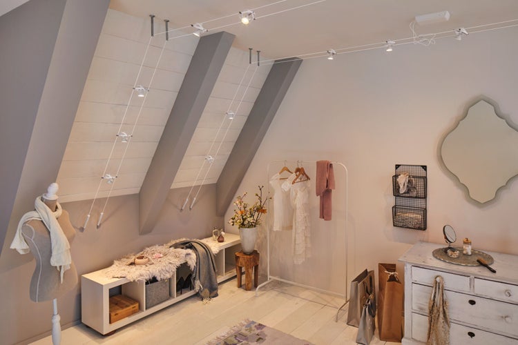 Dachgeschosszimmer mit Seilsystemleuchten, Kleiderständer und Kommode