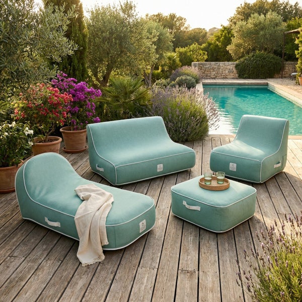 Modernes Set aus gepolsterten Outdoor-Möbeln mit Sofa, Sessel, Liege und Hocker auf einer Holzterrasse an einem Pool im Garten.