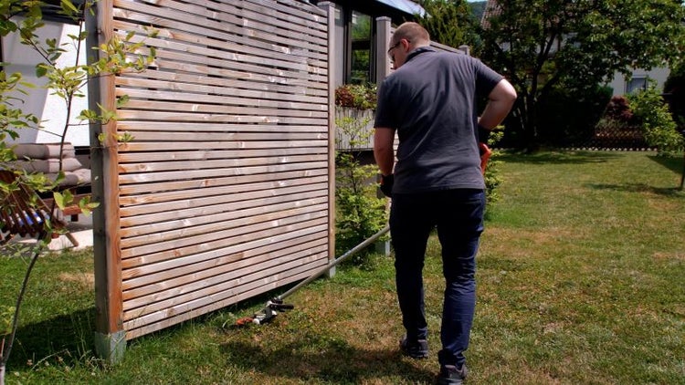 Mann im Garten mit Holzzaun und Rasentrimmer