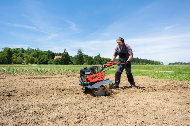 Ein Mann arbeitet mit einer roten AL-KO Motorhacke auf einem Feld zur Bodenbearbeitung unter blauem Himmel.