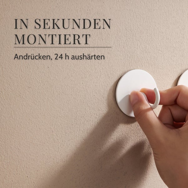 Hand drückt selbstklebenden Wandhaken an eine Wand, Text informiert über Montage und vierundzwanzig Stunden Aushärtungszeit.