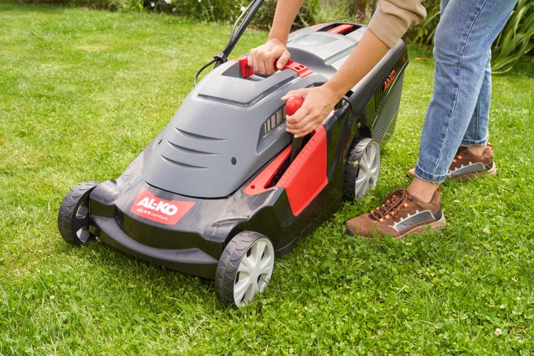 Eine Person benutzt einen AL-KO Elektro-Rasenmäher 40.4 E Comfort zum Mähen des Rasens in einem Garten.