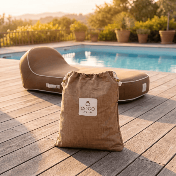 Coco Lounge Logo auf einer Stofftasche für einen Outdoor-Sitzsack auf einer Holzterrasse neben einem Pool und Pflanzen.