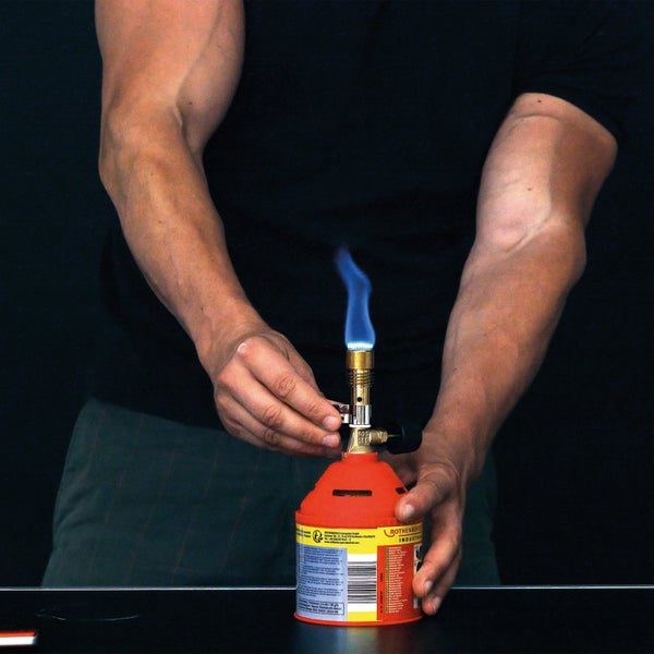 Person hält eine brennende Rothenberger Gaslötlampe mit blauer Flamme in der Hand.