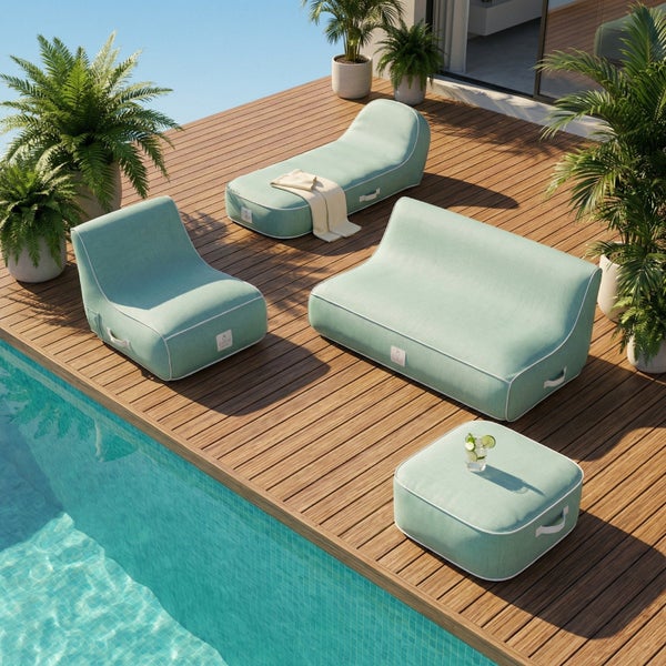 Outdoor-Lounge-Möbelset auf einer Holzterrasse am Pool, bestehend aus Sofa, Sessel, Liege und Hocker mit Stoffbezug sowie Grünpflanzen.