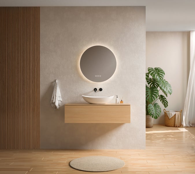 Modernes Badezimmer mit rundem LED Spiegel über einem hängenden Waschtisch aus Holz, weißem Aufsatzwaschbecken und einer Monstera Pflanze.