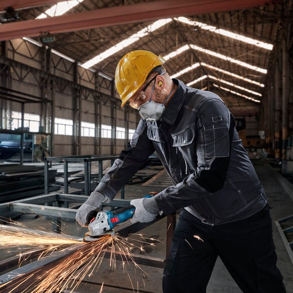Ein Arbeiter in Arbeitskleidung benutzt einen Winkelschleifer in einer Fabrik.